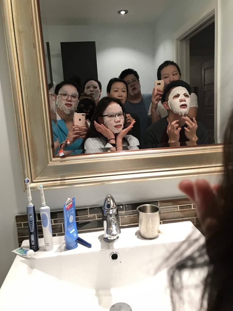 A group of 8 people crammed in a bathroom putting facial sheet masks on after a day of exploring the city.