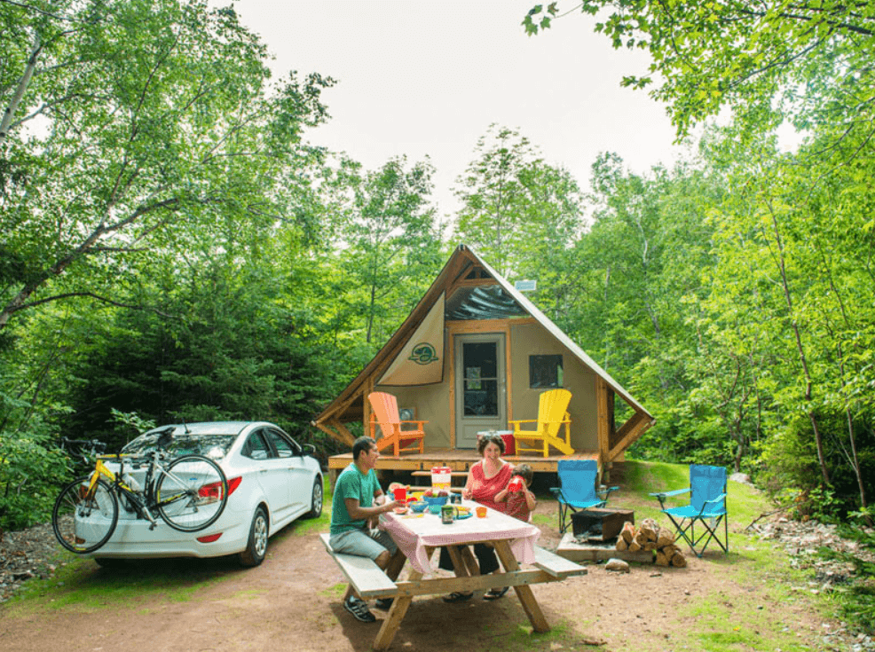 Family enjoying a picnic with a parked car in front of an oTENTiks at Cape Breton Highland National Park