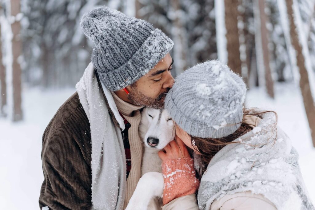 Couple in the snow kissing each other and the dog - Photo by Mikhail Nilov from Pexels to depict dog-friendly romantic getaways