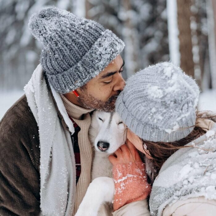 Couple in the snow kissing each other and the dog - Photo by Mikhail Nilov from Pexels to depict dog-friendly romantic getaways